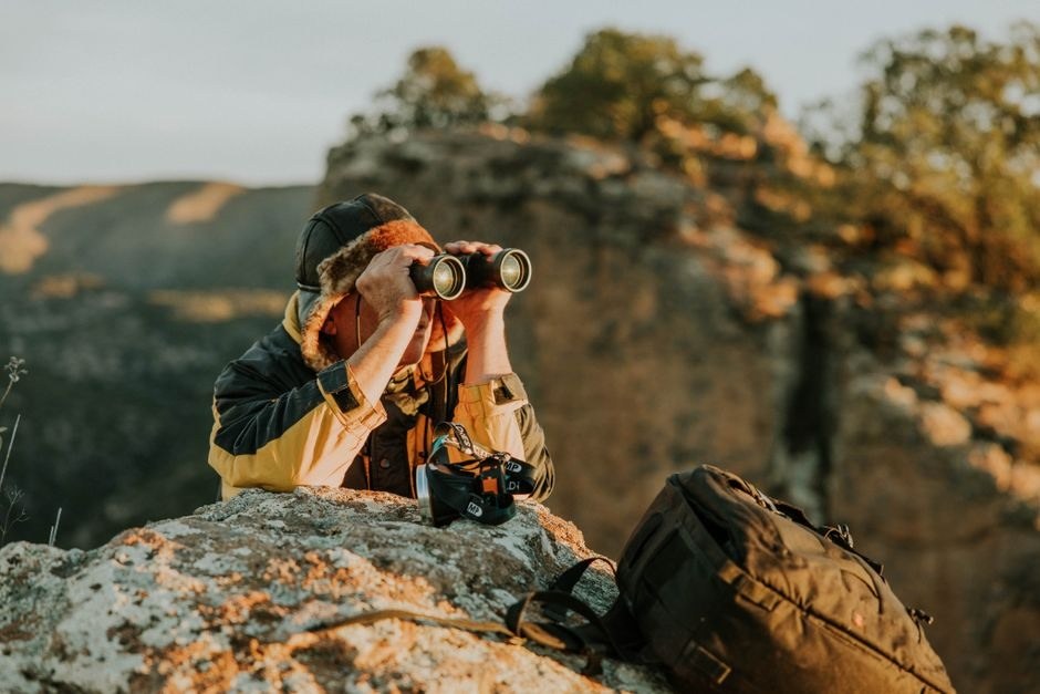 A photographer using a camera from a rocky overlook in the countryside
